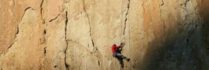 Rock climber in red scaling a steep cliff in natural sunlight, showcasing adventure and outdoor extreme sports.